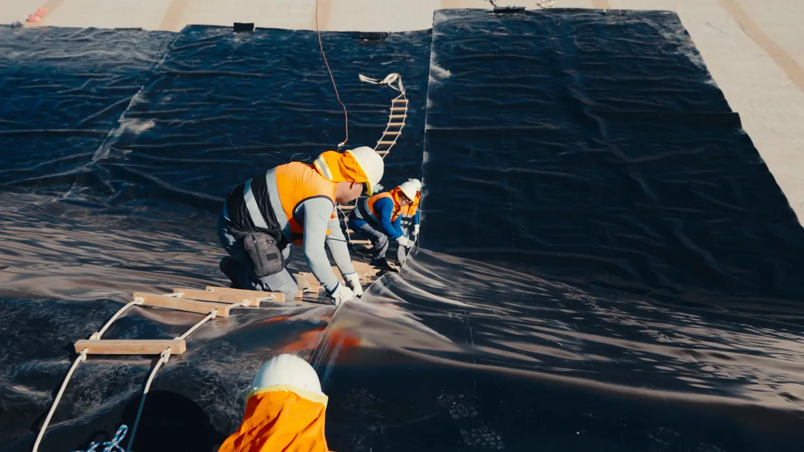 Cuadrilla instalando geomembrana en talud; fotograma real del video de Arauken